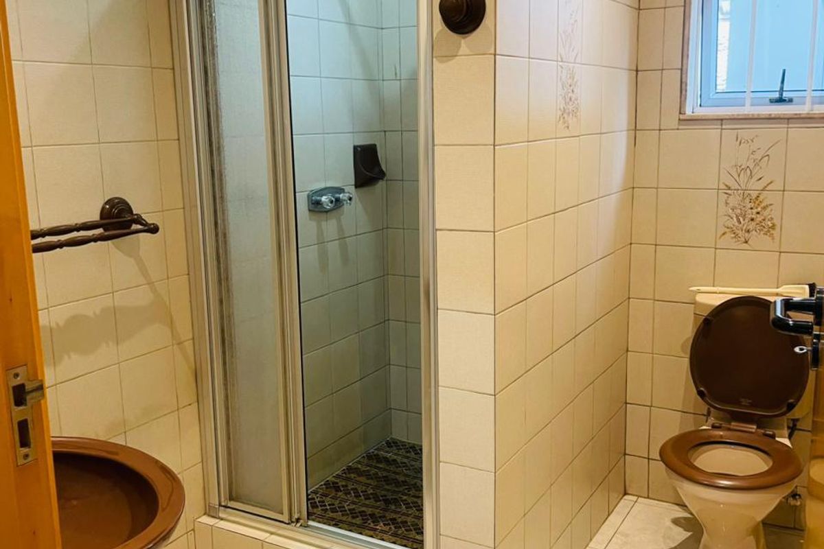A dated bathroom featuring a shower enclosure, toilet, and tiled finishes throughout, offering potential for a modern renovation.