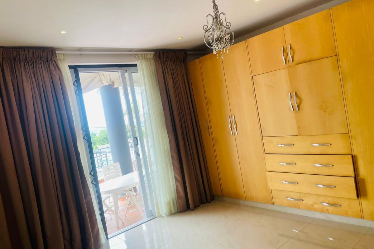 A bright bedroom featuring extensive built-in wooden cabinetry, tiled flooring, and a sliding glass door providing access to an outdoor balcony area.