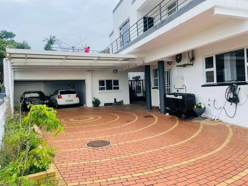 Front exterior view of the apartment building featuring a circular paved driveway, covered garage parking, and an upper-level balcony with metal railings.