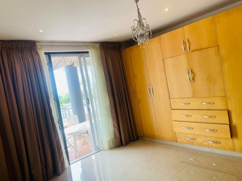 A bright bedroom featuring extensive built-in wooden cabinetry, tiled flooring, and a sliding glass door providing access to an outdoor balcony area.