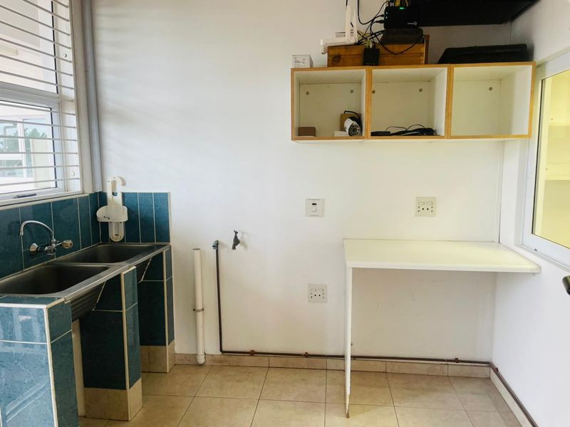 A functional laundry area featuring a double stainless steel sink, tiled splashback, fixed shelving, and plumbing connections for appliances.