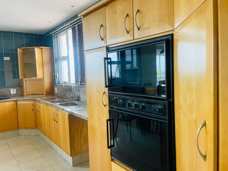 A functional kitchen featuring light wood cabinetry, granite countertops, a double sink, and a built-in oven with a tiled splashback.