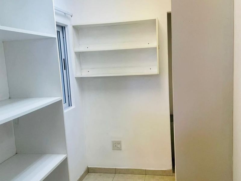 A clean, empty utility space featuring built-in white shelving, tiled flooring, and a functional sliding window, suitable for storage or a home office setup.