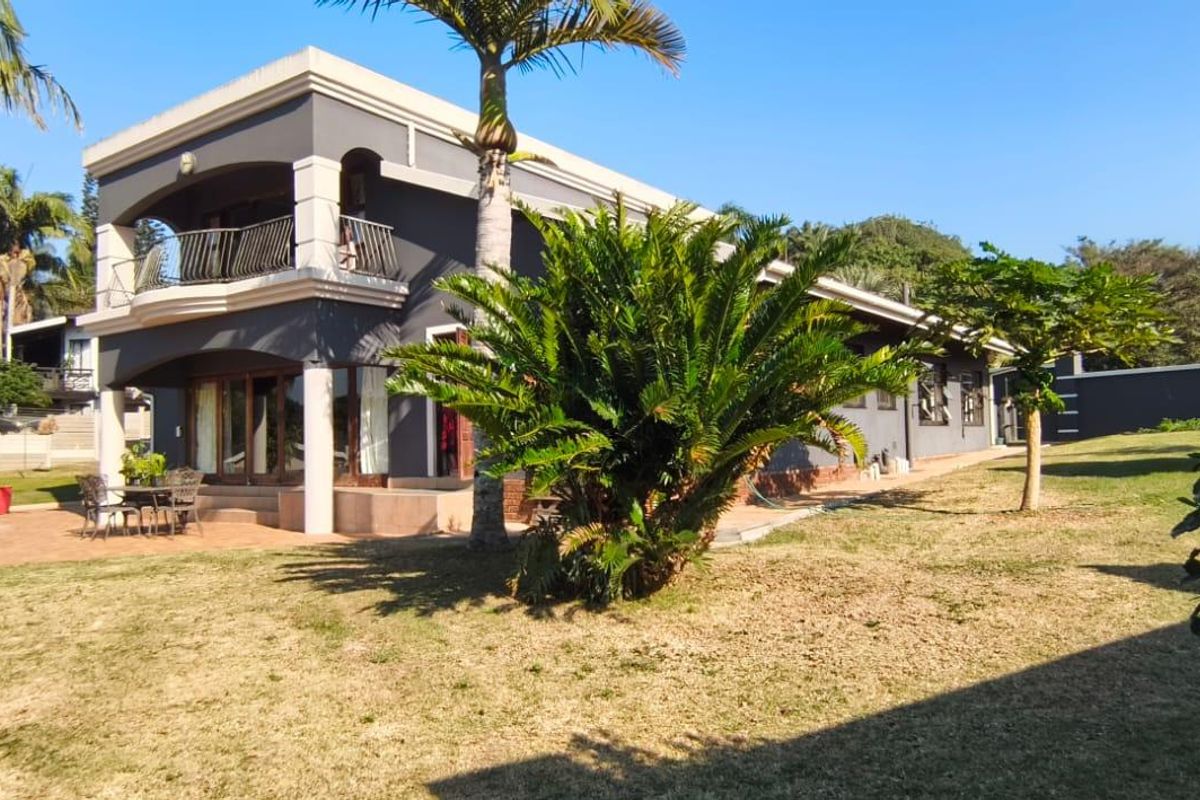 Rear view of a two-story house featuring a paved patio area, a balcony with metal railings, and a swimming pool set in a garden.