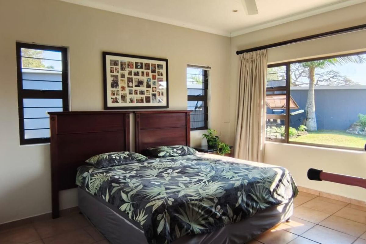 A well-lit bedroom featuring tiled flooring, louver windows, and a ceiling fan, offering a comfortable space with natural light and garden views.