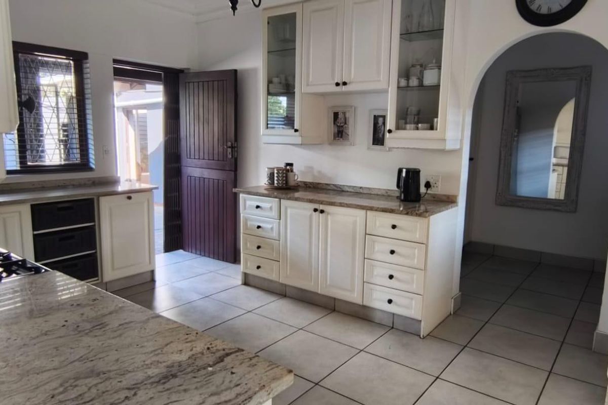 A functional kitchen featuring white cabinetry, granite countertops, a gas hob, and tiled flooring, with an open archway leading to adjacent living spaces.