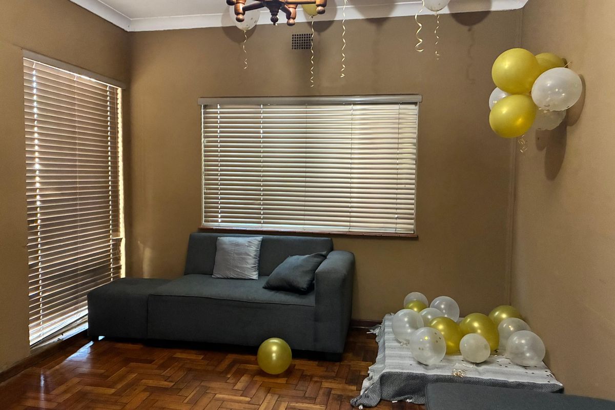 A living room featuring classic parquet flooring, neutral wall tones, and venetian blinds, offering a functional space with traditional architectural details.