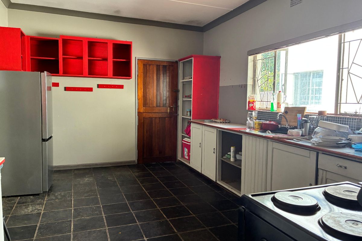 A functional kitchen featuring tiled flooring, built-in cabinetry with open shelving, and a window with security bars, offering potential for modernization.