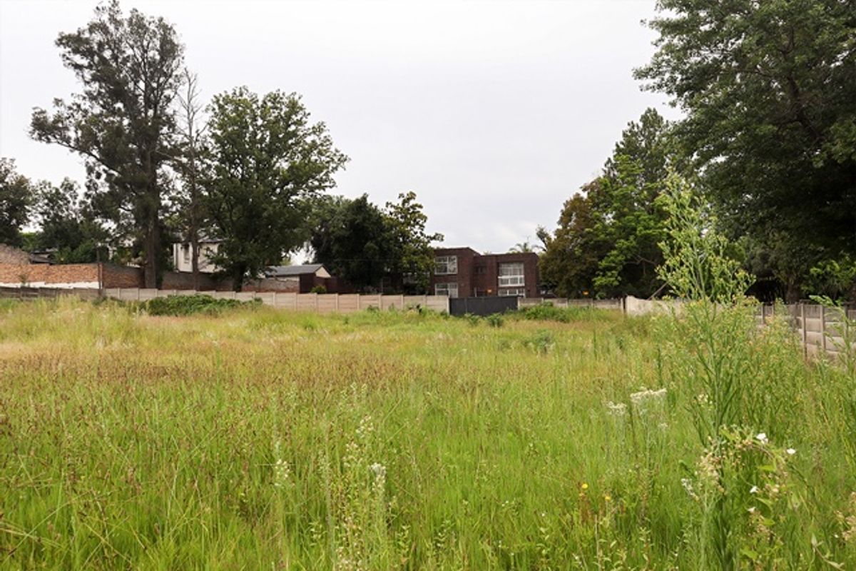 A vacant residential plot featuring overgrown grass and established perimeter boundary walls, offering a blank canvas for future development.