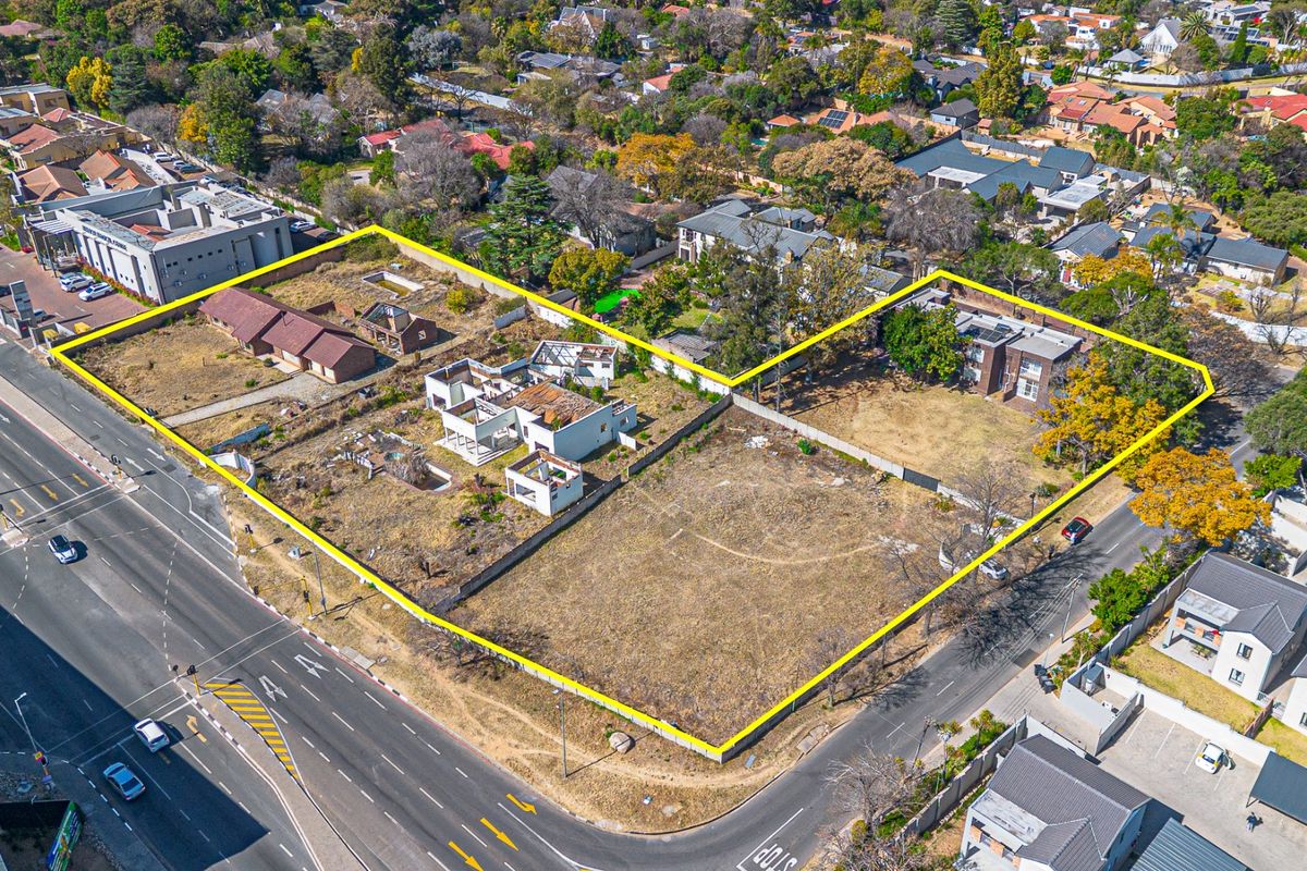 Aerial view of a large vacant residential development site featuring existing dilapidated structures and boundary walls, situated on a prominent corner plot.