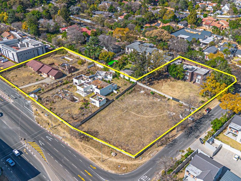 Aerial view of a large vacant residential development site featuring existing dilapidated structures and boundary walls, situated on a prominent corner plot.