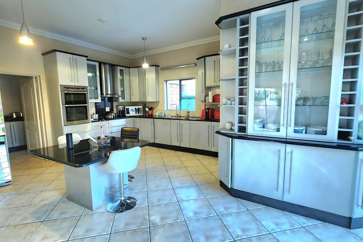 Spacious kitchen featuring modern cabinetry, granite countertops, a central island, and integrated appliances, finished with neutral ceramic floor tiles.