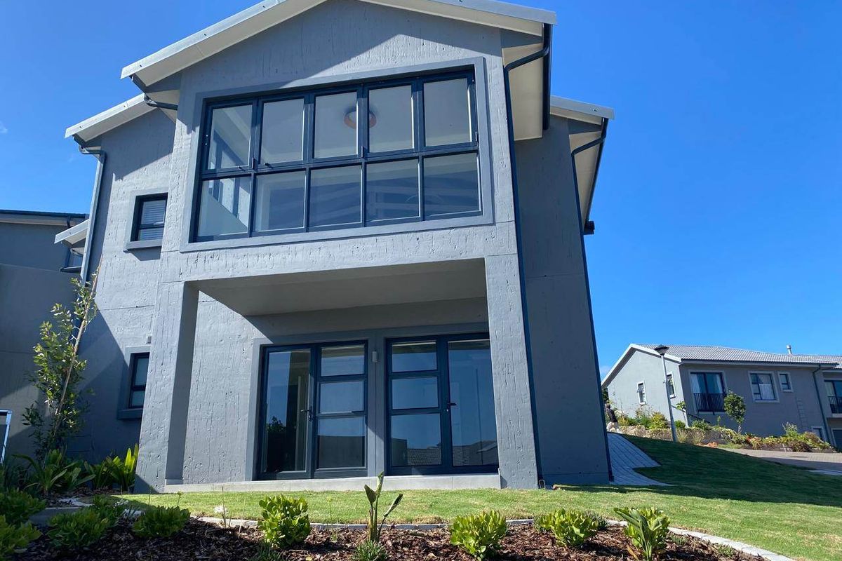 Rear elevation of a modern two-story house featuring dark grey rendered walls, large aluminium-framed windows, and sliding glass doors opening to the garden.