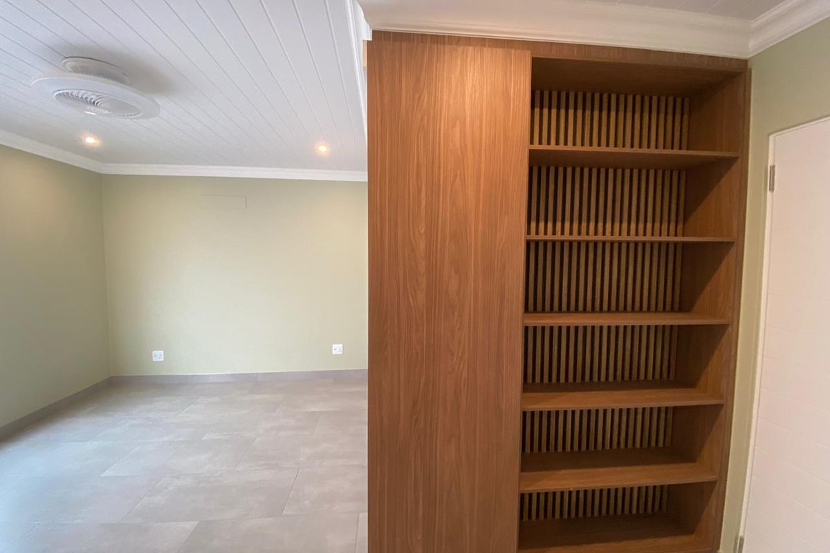 A bright, modern living area featuring neutral tiled floors, a tongue and groove ceiling, and a custom built-in wooden shelving unit.