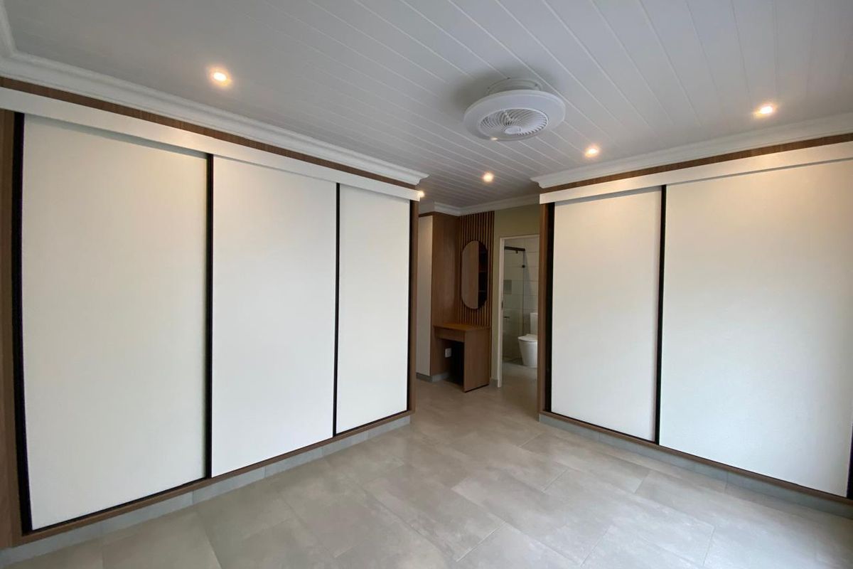 Spacious bedroom featuring extensive built-in sliding door wardrobes, modern tiled flooring, recessed lighting, and an integrated vanity area leading to an en-suite bathroom.