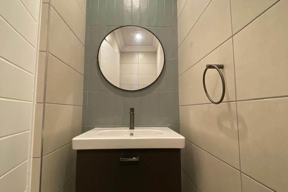 A modern, compact bathroom featuring a wall-mounted vanity with a ceramic basin, mixer tap, and stylish blue-grey tiled feature wall.