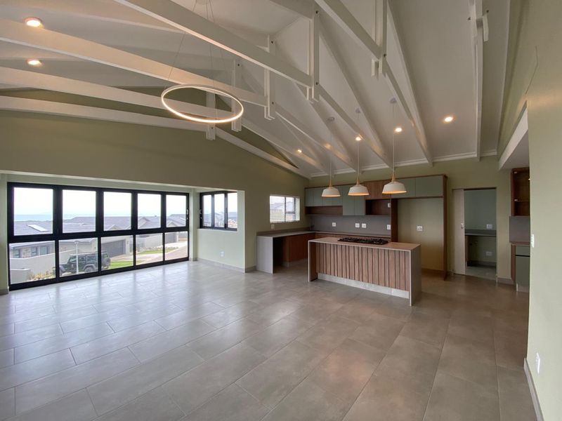 Spacious open-plan living and kitchen area featuring a vaulted ceiling with exposed rafters, modern kitchen island with hob, and large sliding doors.