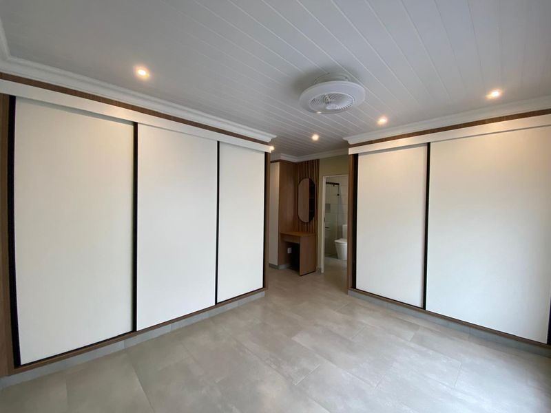 Spacious bedroom featuring extensive built-in sliding door wardrobes, modern tiled flooring, recessed lighting, and an integrated vanity area leading to an en-suite bathroom.