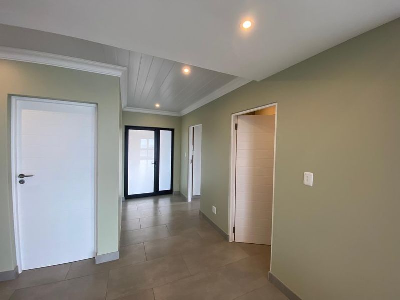 A bright and modern hallway featuring neutral wall tones, tiled flooring, recessed downlighting, and a decorative tongue and groove ceiling panel section.