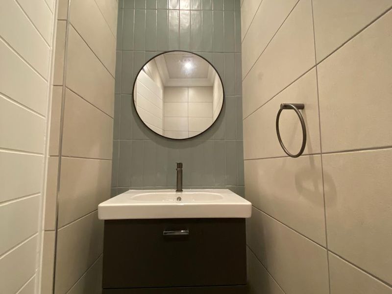 A modern, compact bathroom featuring a wall-mounted vanity with a ceramic basin, mixer tap, and stylish blue-grey tiled feature wall.