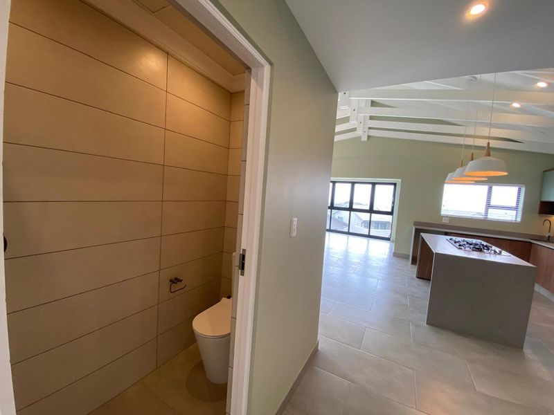 Spacious open-plan living area featuring a modern kitchen island with gas hob, exposed rafters, and an adjacent tiled guest toilet.