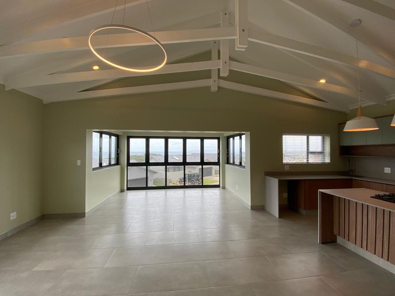 Spacious open-plan living and kitchen area featuring vaulted ceilings with exposed beams, modern tiled flooring, and large windows offering expansive views.