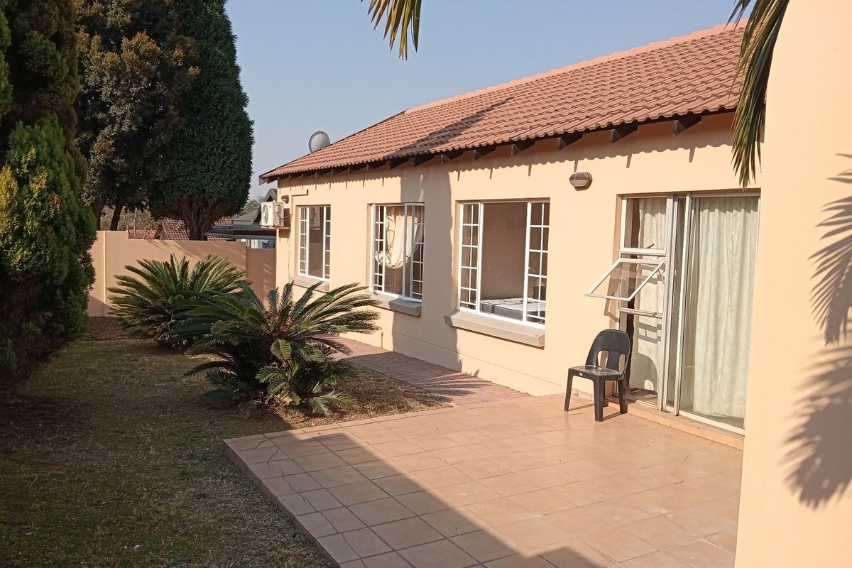 Rear view of the townhouse featuring a paved patio area, sliding glass doors, and a well-maintained garden space.