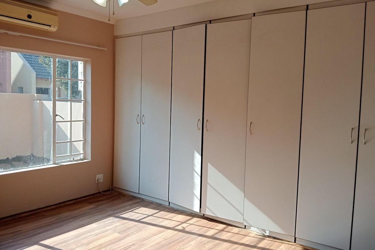 A bright, empty bedroom featuring extensive built-in cupboards, laminate flooring, a ceiling fan, and a wall-mounted air conditioning unit.
