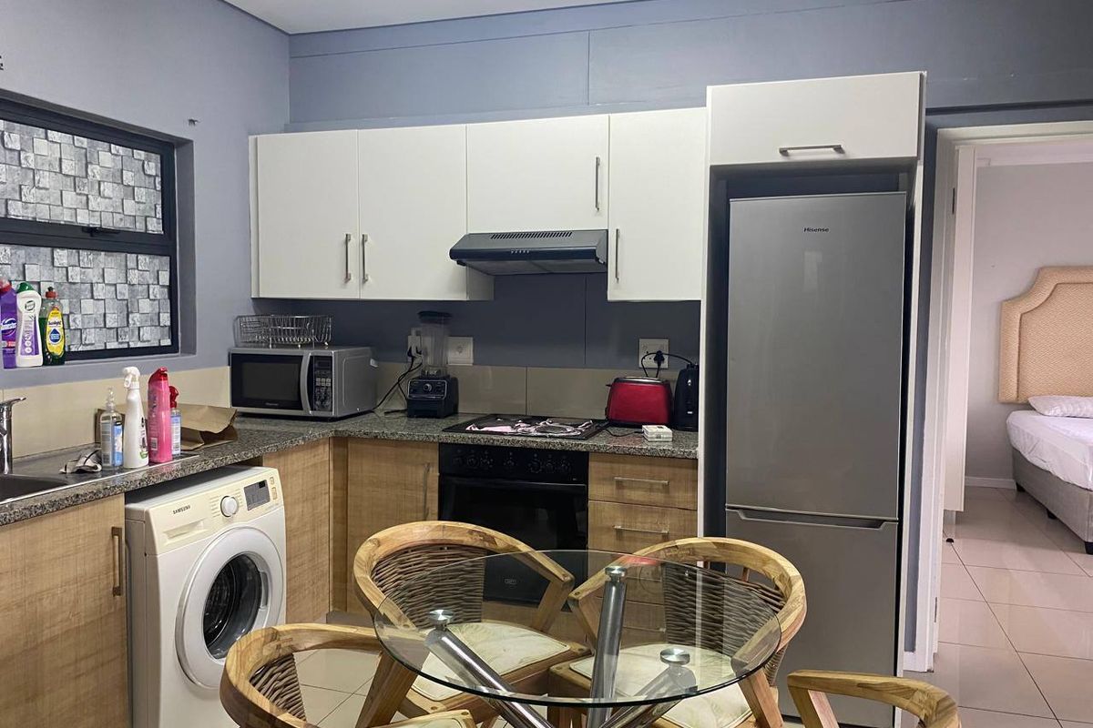 Functional kitchen featuring light wood cabinetry, granite countertops, built-in oven with gas hob, extractor fan, and integrated laundry plumbing.