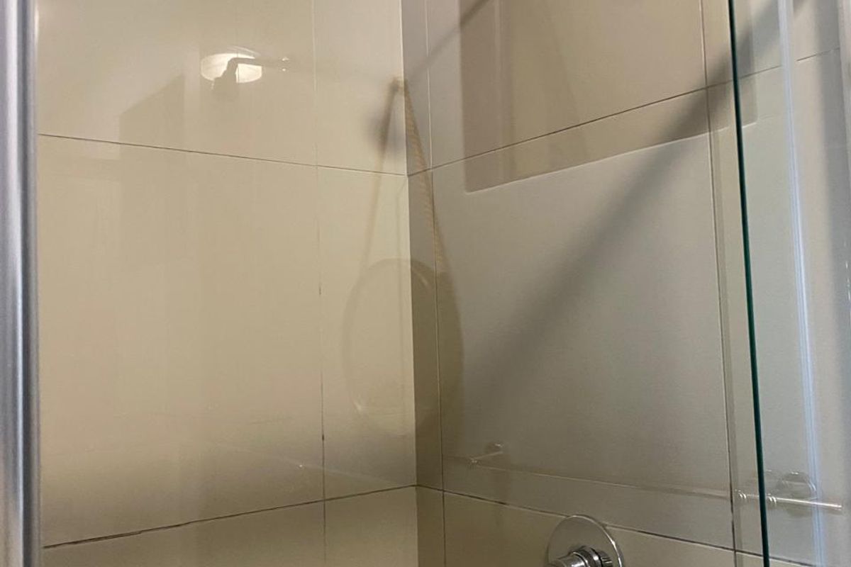 A clean, modern shower enclosure featuring neutral ceramic wall tiles, a chrome shower mixer, and a fixed shower head.
