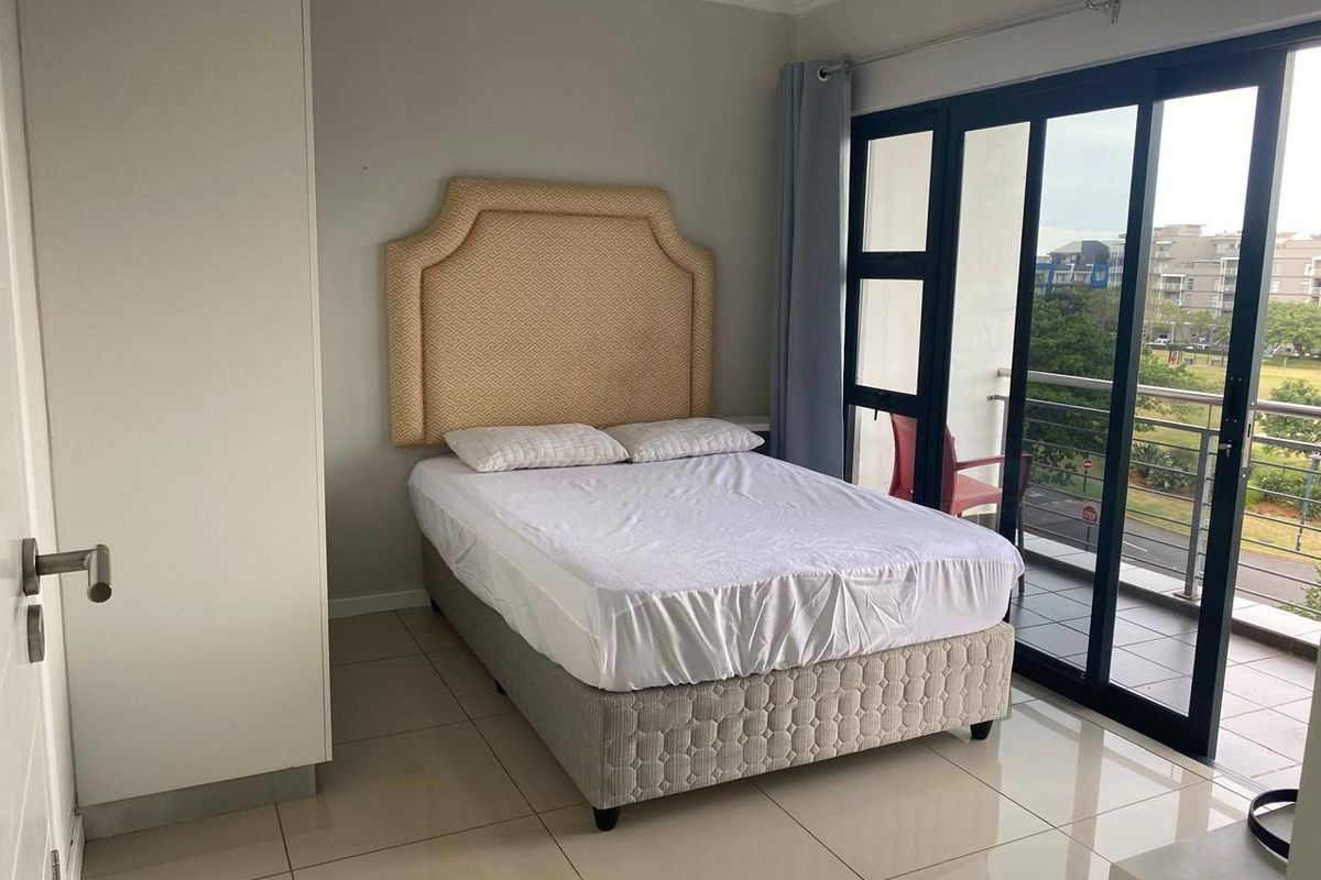 A bright bedroom featuring tiled flooring, a built-in wardrobe, and large sliding glass doors providing access to a private balcony.