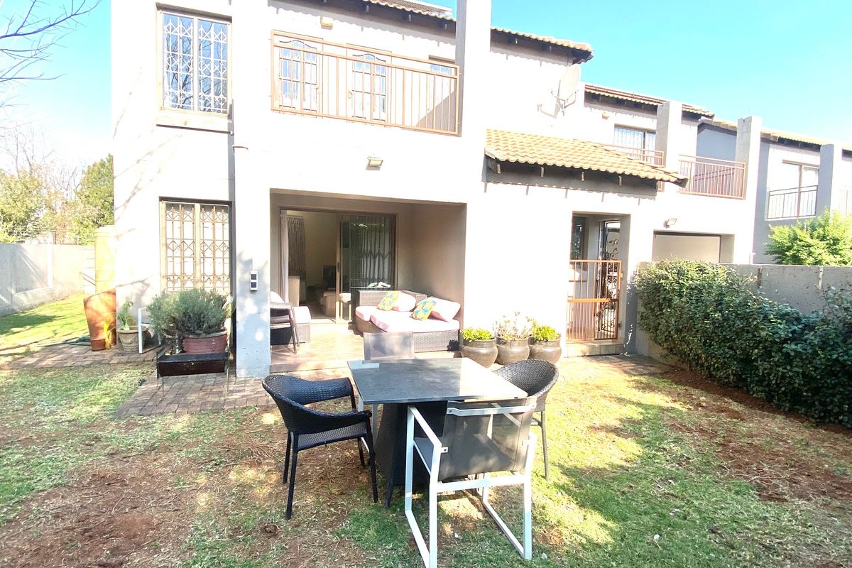 Rear view of the townhouse featuring a covered patio, small garden, and upper-level balcony with security features.