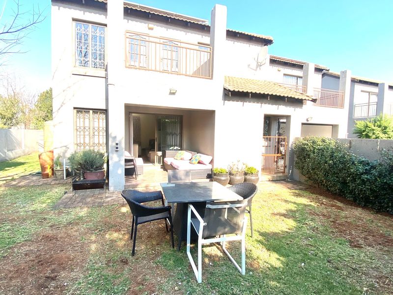 Rear view of the townhouse featuring a covered patio, small garden, and upper-level balcony with security features.