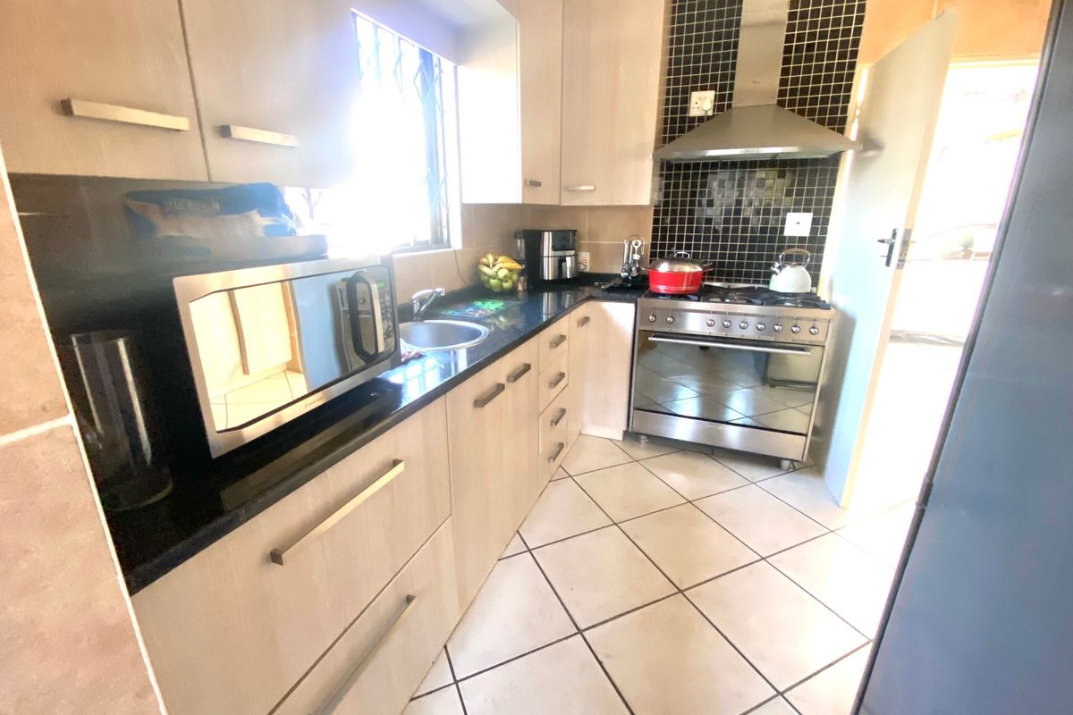 A functional kitchen featuring light wood cabinetry, granite countertops, a stainless steel gas stove with extractor fan, and tiled flooring.