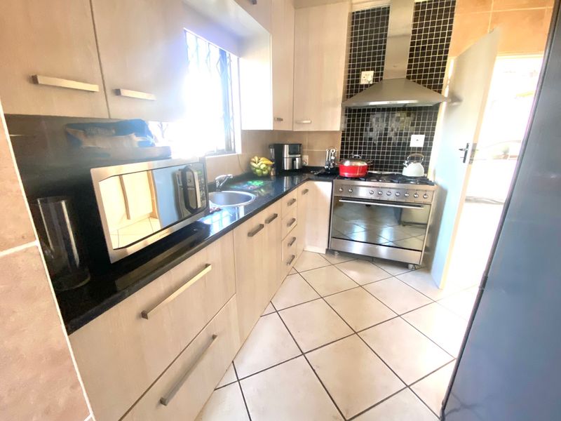 A functional kitchen featuring light wood cabinetry, granite countertops, a stainless steel gas stove with extractor fan, and tiled flooring.