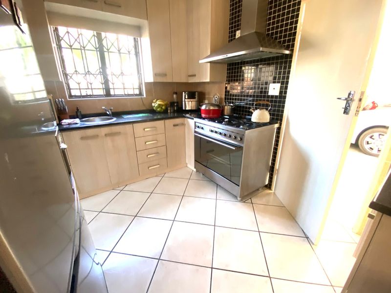 Functional kitchen featuring light wood cabinetry, stainless steel gas stove with extractor fan, tiled backsplash, and tiled flooring.