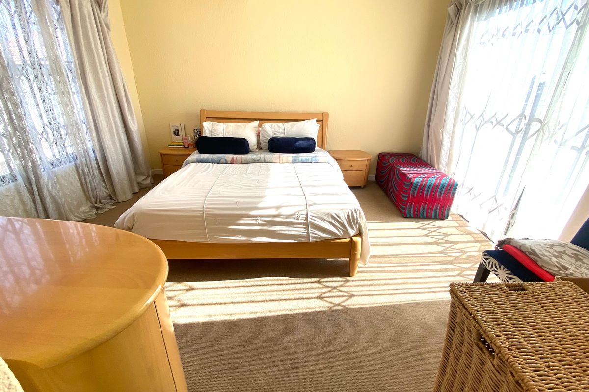 A well-lit bedroom featuring neutral carpeted flooring, a wall-mounted split-system air conditioner, and large sliding glass doors providing access to the exterior.