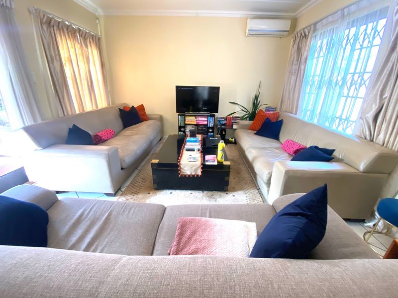 A comfortable living room featuring tiled flooring, cornicing, and a wall-mounted air conditioning unit, with security gates on the windows.
