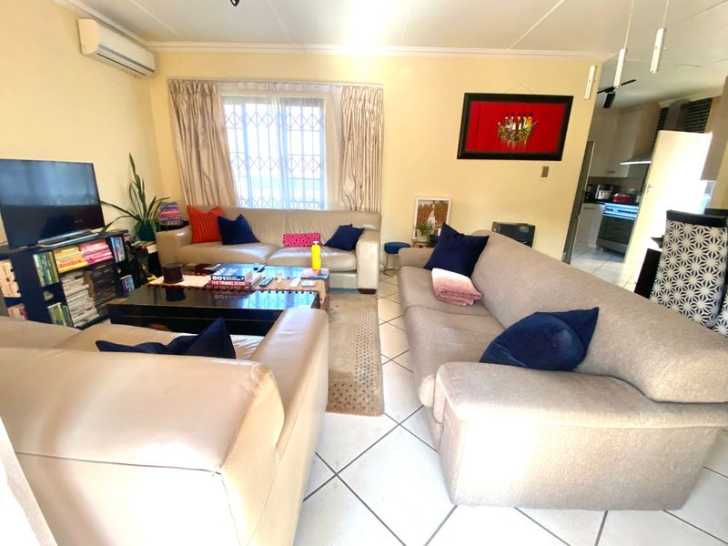 Open plan living area featuring tiled flooring, coving, and a wall-mounted air conditioning unit, with a view into the adjacent kitchen space.