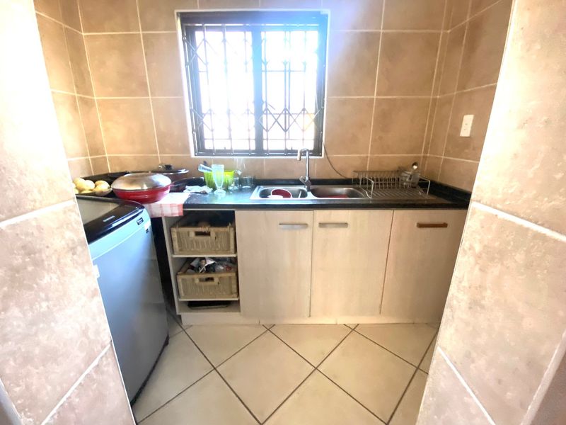 A functional scullery area featuring a double sink, granite countertops, built-in cabinetry, and tiled finishes, providing a practical space for kitchen preparation and wash-up.