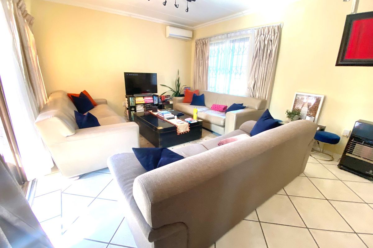 A comfortable living room featuring ceramic tile flooring, a wall-mounted air conditioning unit, and track lighting, providing a functional space for relaxation.