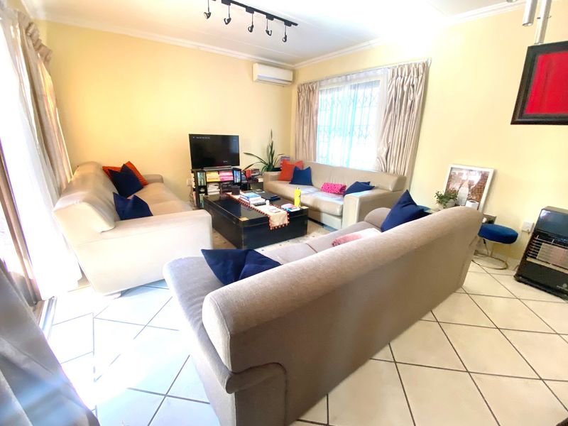 A comfortable living room featuring ceramic tile flooring, a wall-mounted air conditioning unit, and track lighting, providing a functional space for relaxation.
