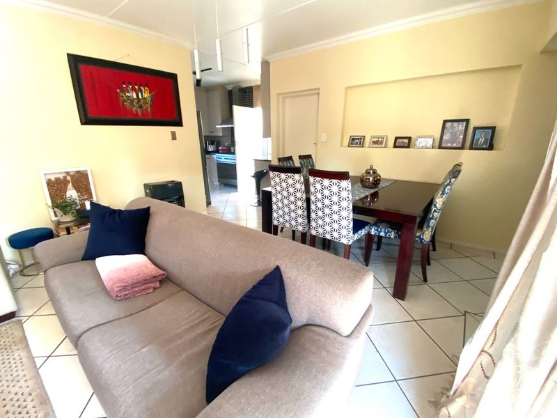 Open plan living and dining area featuring tiled flooring, a recessed wall niche, and coved ceiling cornices, with an adjacent kitchen visible in the background.
