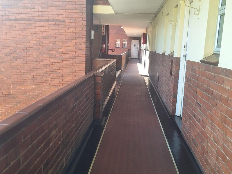 An exterior apartment building walkway featuring brick walls and a covered corridor.