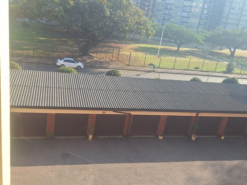 An elevated view of a row of garages with corrugated roofing and asphalt driveway, situated within an apartment complex.