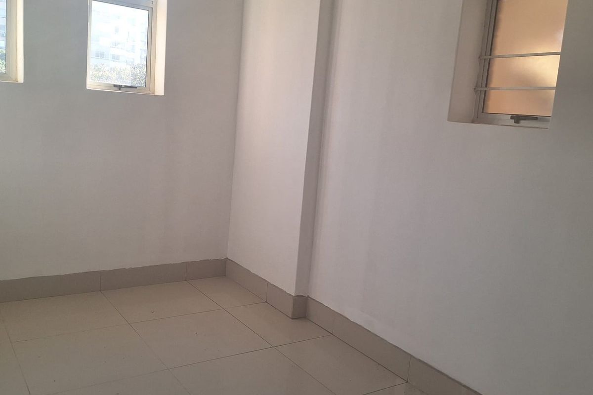 A bright, empty bedroom featuring neutral tiled flooring and multiple windows with security bars, offering a clean canvas for personalization.