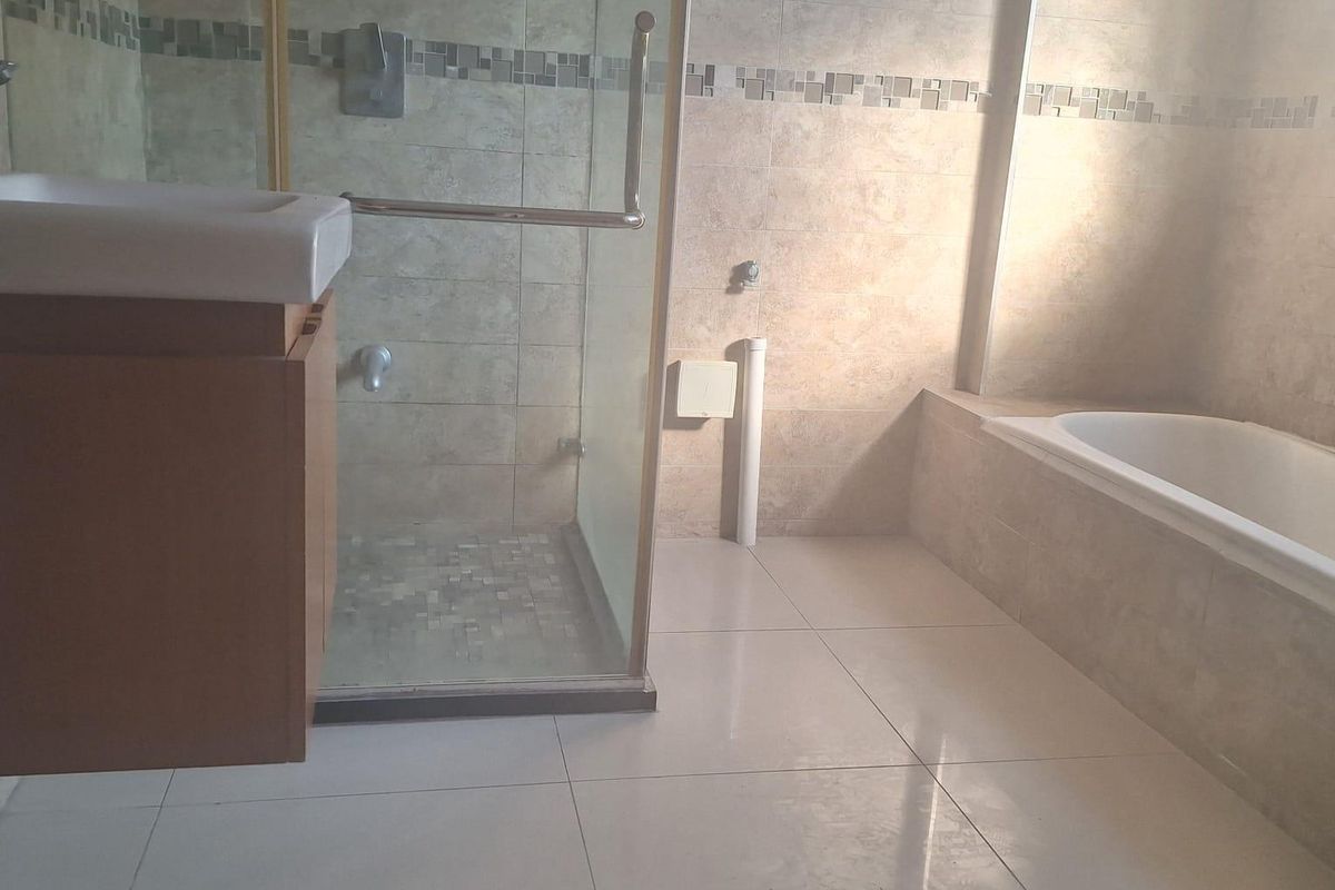 A spacious bathroom featuring a glass-enclosed shower, a built-in bathtub, and a wall-mounted vanity with neutral ceramic tiling throughout.