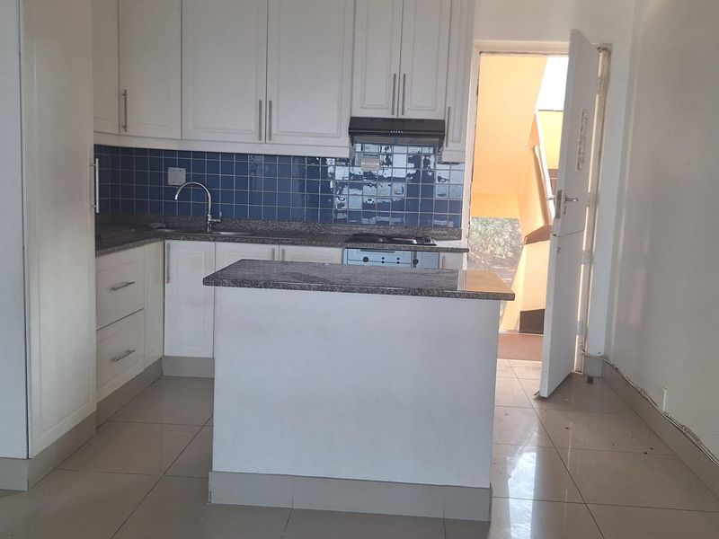 A clean, empty kitchen featuring white cabinetry, granite countertops, a blue tiled backsplash, and a central island with a built-in hob.