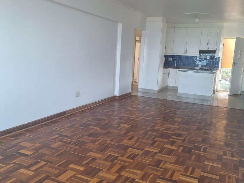 Spacious open-plan living area featuring classic parquet flooring, decorative crown molding, and a functional kitchen with white cabinetry and tiled backsplash.