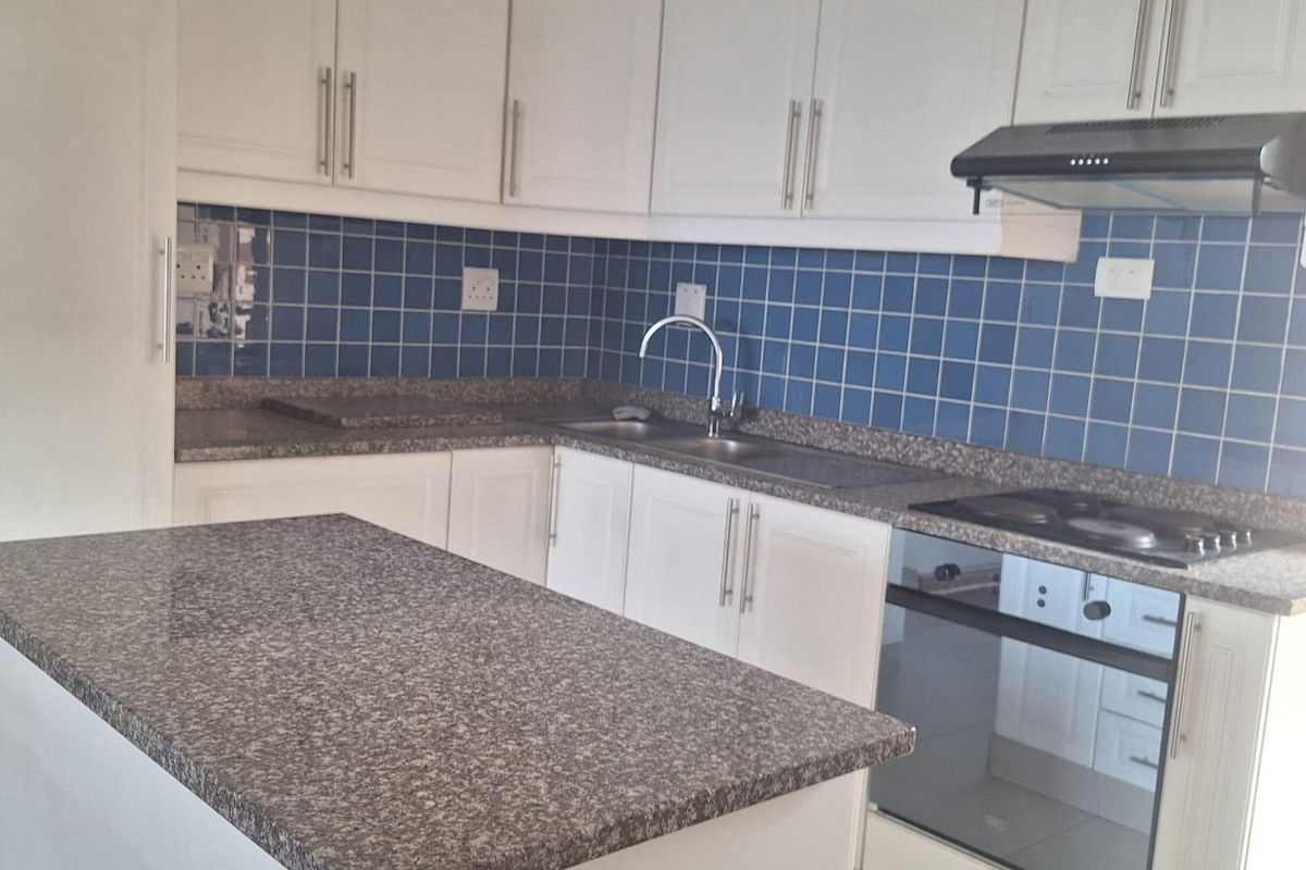 A clean, functional kitchen featuring white cabinetry, granite countertops, a blue tiled backsplash, and integrated appliances including an oven and hob.